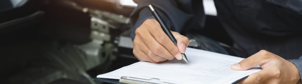 A close-up of a person’s hands writing on a checklist attached to a clipboard, with a blurred mechanical or automotive background. Superior Tire: Tire Shop and Auto Repair Near Me | Barrie | Danforth | Downsview | Markham | Mississauga | Oak Ridges | Scarborough | Thornhill | Toronto | https://superiortire.ca/