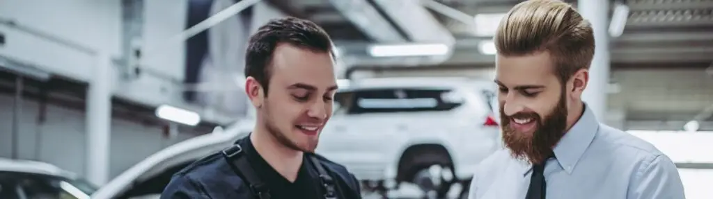 Two men standing in an auto repair shop, one in a mechanic uniform and the other in business attire, smiling and looking down at a clipboard together. A car on a lift is visible in the background. Superior Tire: Tire Shop and Auto Repair Near Me | Barrie | Danforth | Downsview | Markham | Mississauga | Oak Ridges | Scarborough | Thornhill | Toronto | https://superiortire.ca/